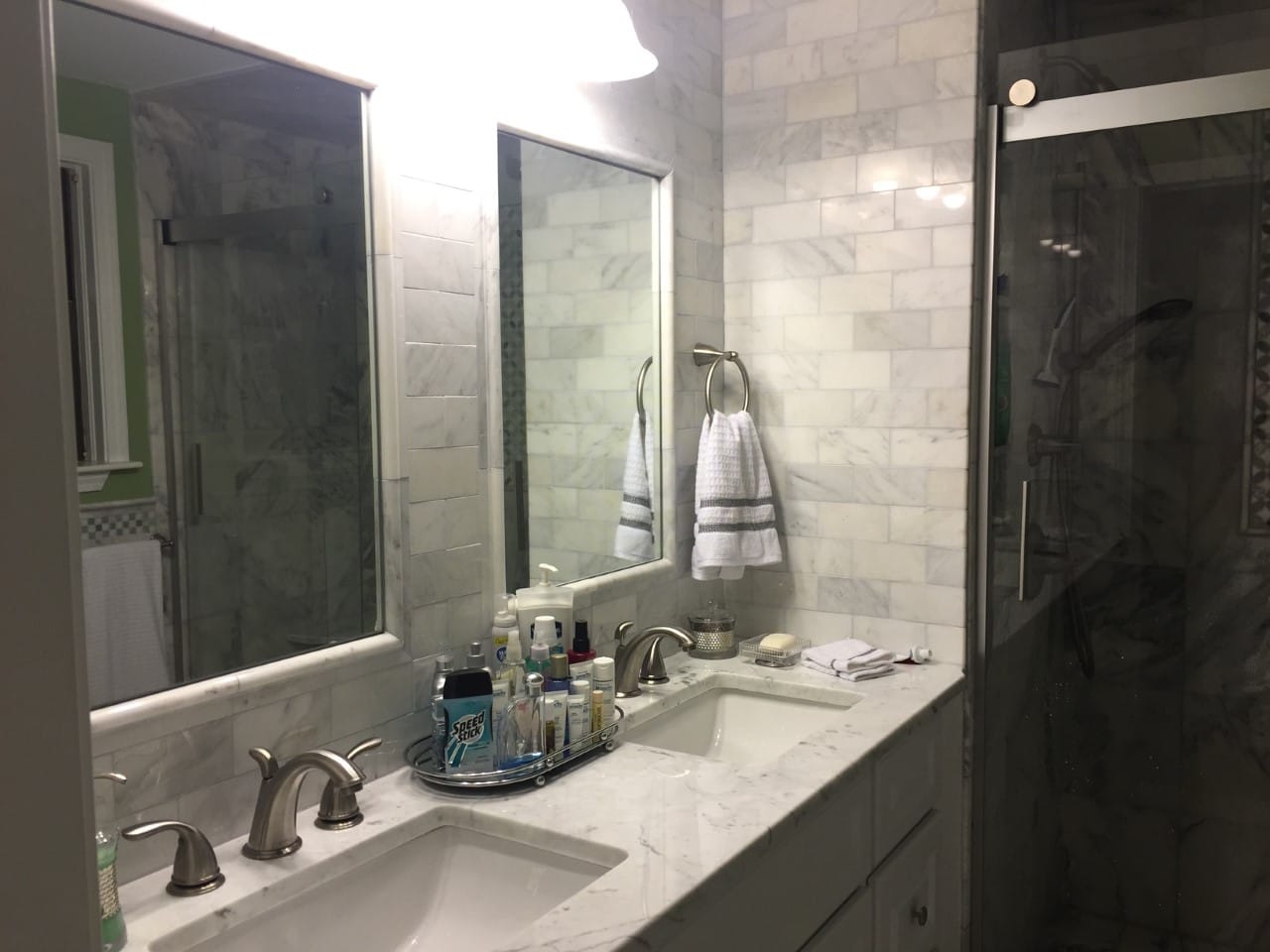 Tiled bathroom vanity wall with two mirrors, a double sink and an adjacent glass shower enclosure