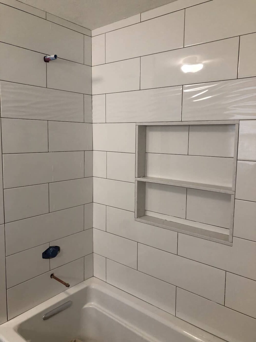Tub surround during installation with large rectangular wall tiles and a wide two-level recessed niche