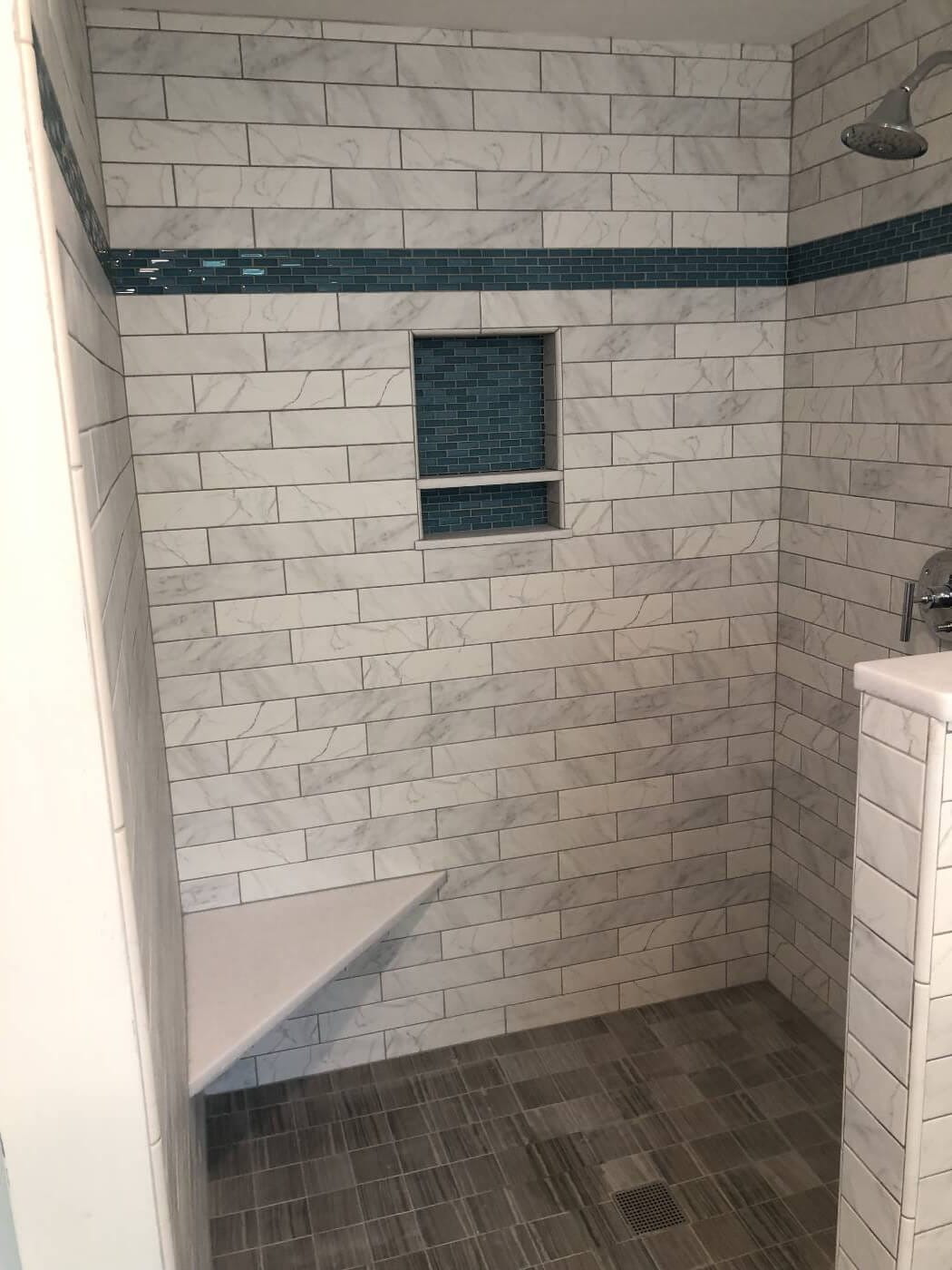 Shower with blue accent tile, a matching two-level niche, a corner bench and a tiled floor